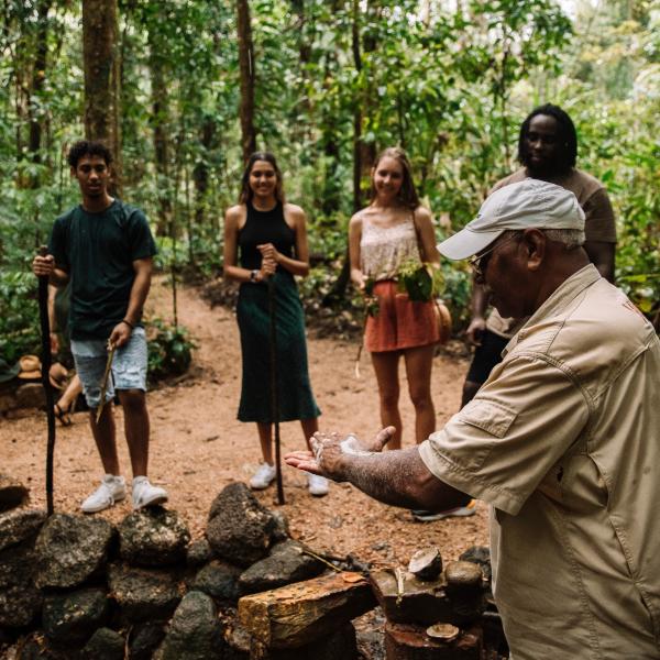 An Indigenous guide demonstrates traditional plant uses to a small group of hikers along a lush rainforest trail, Mossman Gorge, Queensland © Tourism and Events Queensland and Katie Purling