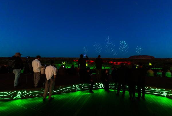 Spectators watch glowing drones light up the night sky above the desert horizon near Uluru during the immersive Wintjiri Wiru experience by Voyages Indigenous Tourism Australia, Northern Territory. © Getty Images for Voyages Indigenous Tourism Australia