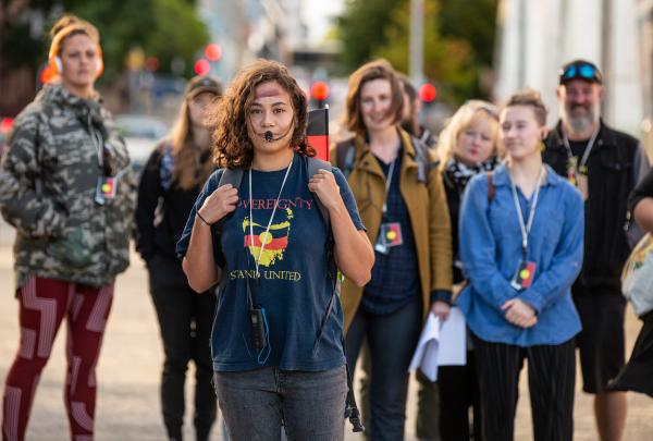An Aboriginal guide wearing a headset leads a group of attentive walkers through urban streets during a walking experience by Blak Led Tours, Hobart, Tasmania.© Jillian Mundy