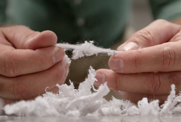 Hands examine shredded white recycled textile fibres above a scattered pile of material, demonstrating sustainable fabric recovery processes. © BlockTexx