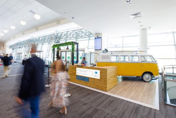 People walking past a retro yellow Kombi van and wooden service desk inside the bright, sunlit concourse of Gold Coast Convention and Exhibition Centre, Gold Coast, Queensland. © Gold Coast Convention and Exhibition Centre