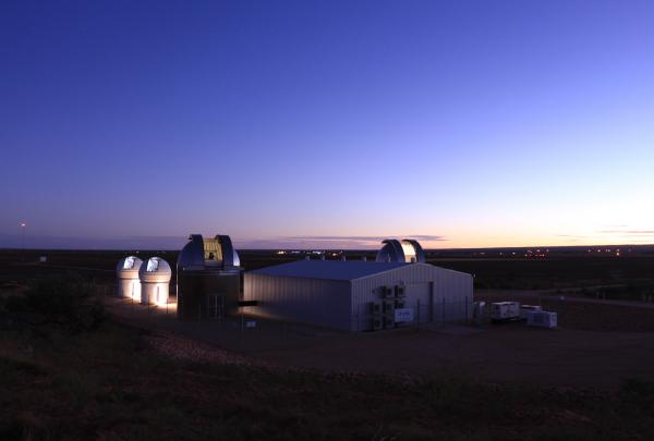 Illuminated astronomical observatory domes glow softly against a deep twilight sky over the remote Outback landscape. © EOS Space Systems