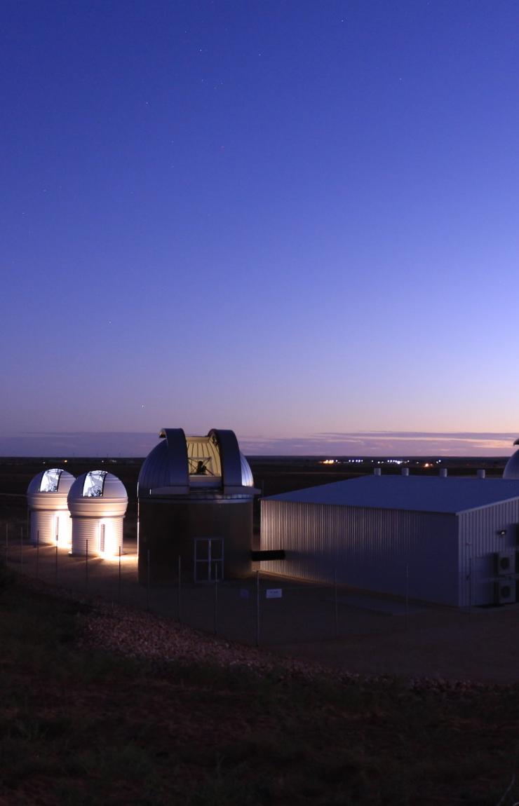 Illuminated astronomical observatory domes glow softly against a deep twilight sky over the remote Outback landscape. © EOS Space Systems