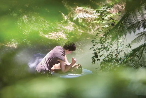 A therapist performs a relaxing spa massage treatment on a client surrounded by lush green rainforest foliage at Jindii Eco Spa in Canberra, Australian Capital Territory, with soft natural light. © VisitCanberra