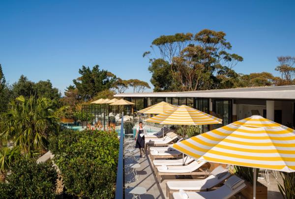 Yellow-and-white striped umbrellas shade poolside loungers on a sunlit resort terrace fringed by lush coastal greenery, Bannisters by the Sea, Shoalhaven, New South Wales. © Justin Alexander