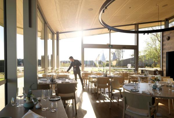 Sunlight streams into an elegant dining room as a waiter sets round tables beside floor-to-ceiling windows, Laura at Point Leo Estate, Mornington Peninsula, Victoria. © Point Leo Estate