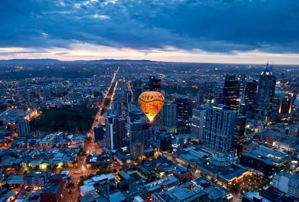 An illuminated hot air balloon by Global Ballooning Australia drifts above the Melbourne city skyline in Victoria at twilight, taking in panoramic views of grid streets and high-rise towers. © Global Ballooning Australia