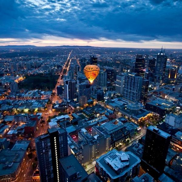 An illuminated hot air balloon by Global Ballooning Australia drifts above the Melbourne city skyline in Victoria at twilight, taking in panoramic views of grid streets and high-rise towers. © Global Ballooning Australia