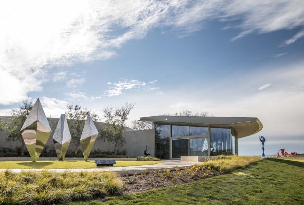 Geometric metallic sculptures glint on manicured lawns outside the modern entrance building under a soft cloudy sky at Pt. Leo Estate on the Mornington Peninsula in Victoria. © Pt Leo Estate
