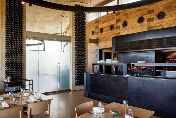 Elegant dining tables set with fine glassware surround a sleek open kitchen counter inside Laura Restaurant at Pt. Leo Estate, Mornington Peninsula, Victoria, framed by floor-to-ceiling wine racks. © Pt Leo Estate