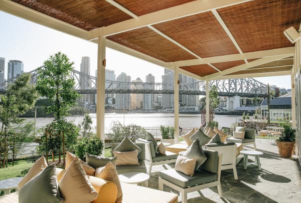 Sunlit outdoor lounge at Howard Smith Wharves in Brisbane, Queensland, featuring cushioned seating beneath a thatched roof looking out over the river toward Story Bridge and the city skyline. © Howard Smith Wharves