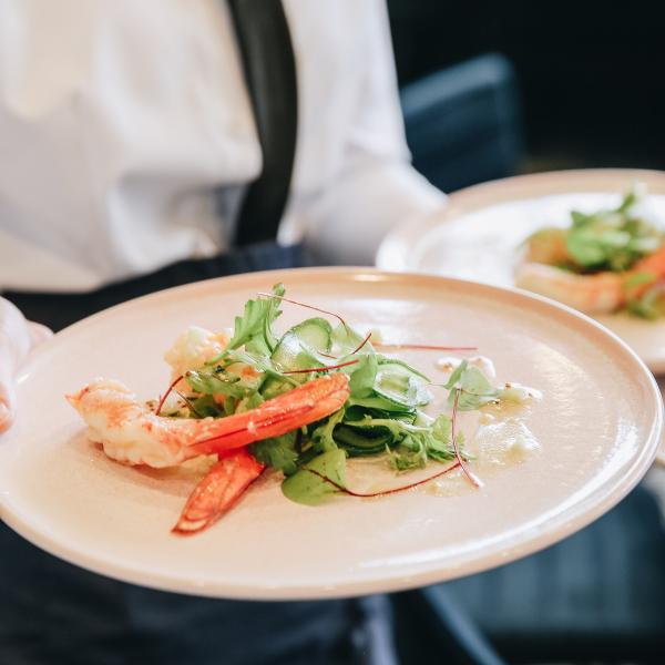 A waiter holds plates with fresh prawns and green salad, demonstrating fine dining service at Howard Smith Wharves in Brisbane, Queensland, surrounded by a stylish, contemporary restaurant setting. © Howard Smith Wharves