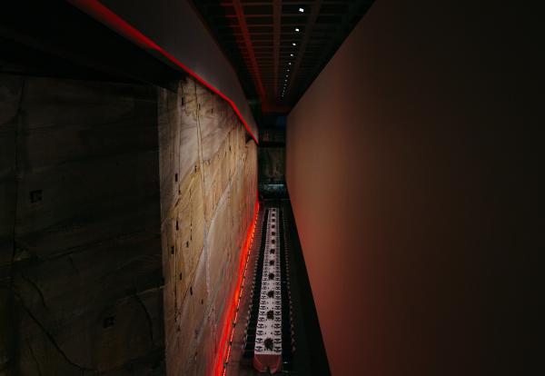 A long banquet table set for a formal event stretches far below along a dramatic sandstone wall lit in glowing red, The Void, MONA, Hobart, Tasmania. © Two Blushin Pilgrims