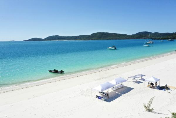 White marquees and boats line pristine white silica sand beside vibrant turquoise water of Whitehaven Beach, Whitsundays, Queensland.© Ocean Dynamics & Affinity Events Whitsundays