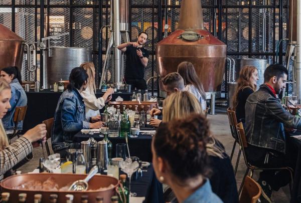 Guests enjoy an interactive spirit workshop at Archie Rose in Rosebery, New South Wales, seated at long tables with cocktail equipment set against towering copper stills and metal mesh walls. © Archie Rose Distilling Co.