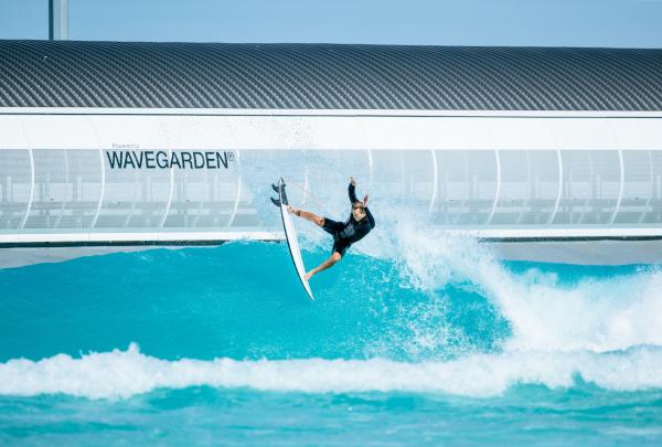 A surfer leaps into the air off a turquoise wave at URBNSURF Melbourne in Victoria, with spray flying against the sleek Wavegarden structure behind. © URBNSURF