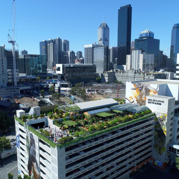 A vibrant rooftop urban farm with lush gardens and greenhouses sits atop a car park structure set against the Melbourne Convention and Exhibition Centre and city skyline, Melbourne, Victoria. © Skyfarm
