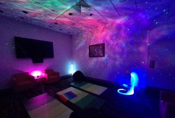 A dimly lit sensory room featuring glowing colourful galaxy lights, soft floor mats, and armchairs at the Brisbane Convention and Exhibition Centre, Brisbane, Queensland. © Tourism Australia