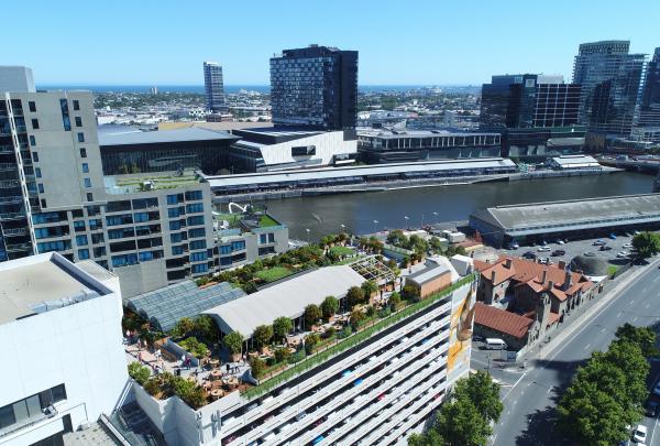 An aerial view shows a sprawling rooftop urban farm and greenhouse atop the multi-storey Skyfarm building along the Yarra River, Melbourne, Victoria. © Skyfarm