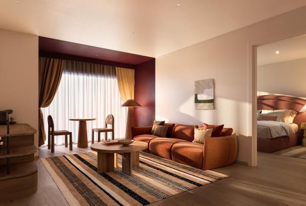 The stylish hotel lounge room at Hyde Perth in Western Australia features a plush terracotta sofa, a striped area rug, a round timber coffee table, and a small dining setting by the window. An open doorway reveals the main bedroom. © Hyde Perth