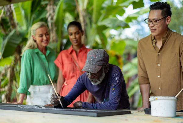 Three guests watching as an Indigenous artist paints. © Jason Ierace