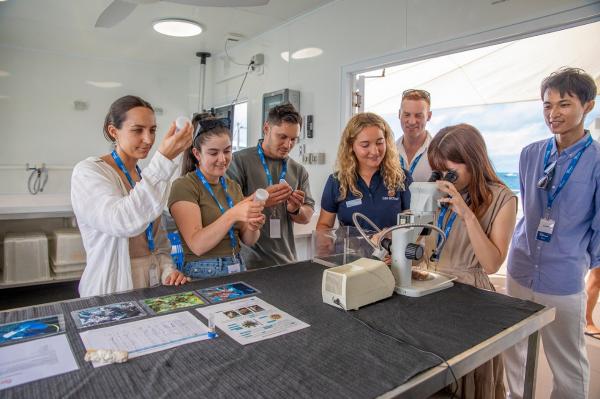 A group of people standing in a lab gather around a microscope. © Reef Unlimited/GBR Biology