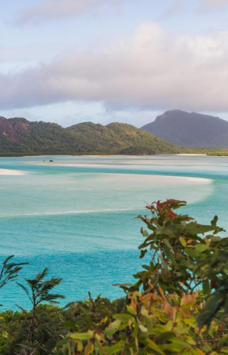 Swirling white sands blend with clear turquoise ocean waters beneath green hills in an elevated view of Hill Inlet, Whitsundays, Queensland © Tourism Australia