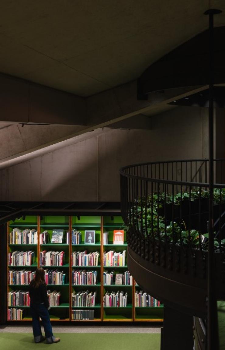 Above a dimly-lit subterranean library room sits a mezzanine, with a tree at its centre. © MONA/Jesse Hunniford