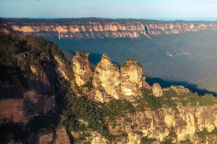 An aerial shot captures the iconic Three Sisters rock formation in Katoomba, bathed in the warm afternoon sunshine © Tourism Australia