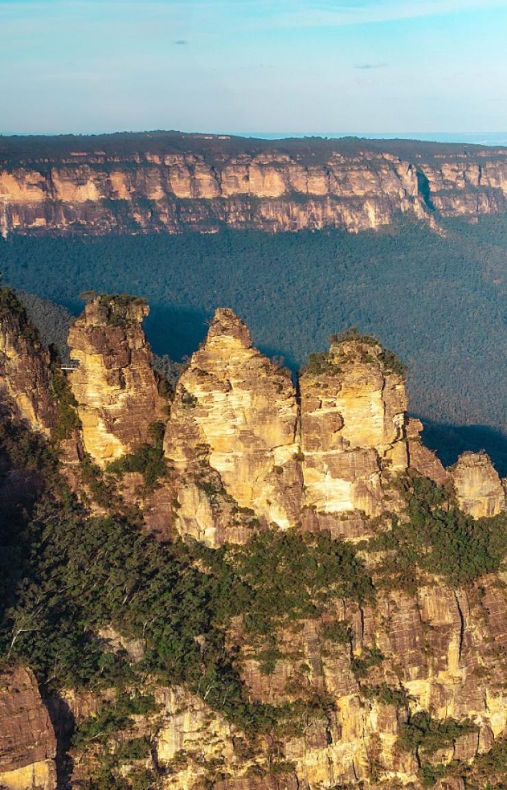 An aerial shot captures the iconic Three Sisters rock formation in Katoomba, bathed in the warm afternoon sunshine © Tourism Australia