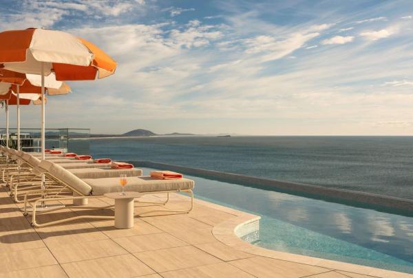 A rooftop pool with lounge chairs, orange and white umbrellas, sat facing the uninterrupted views over the ocean. © Rhiannon Taylor / Avani Mooloolaba Beach Hotel