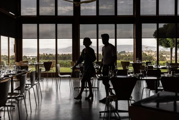 Two people walk through a large, glass-clad restaurant overlooking a winery and the nearby mountainous landscape © Tourism Australia
