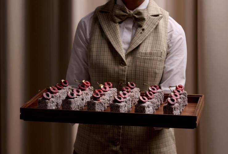 Wait staff holding a tray of upscaled lamingtons, The Lands by Capella, Bridge Street Sydney, New South Wales © Esteban La Tessa 251201 The Lands by Capella F&B Shoot5620