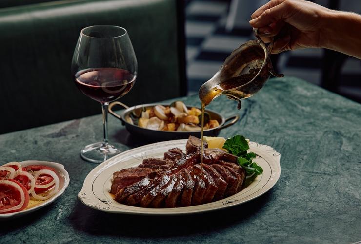 T-Bone Steak Pour, a plate of vegetables, tomato salad and red wine at Osteria Mucca, Sydney, New South Wales © Osteria Mucca