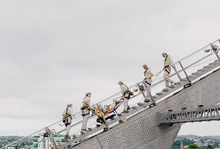 A group climbs the Story Bridge on on the Accessible Bridgeclimb with a guest in the custom stairclimber wheelchair, Brisbane, Queensland © Story Bridge Adventure Climb