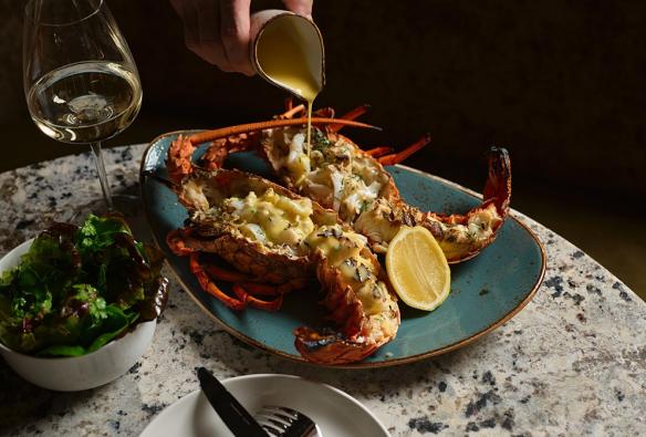Grilled Eastern Rock Lobster in a platter with Pernod Beurre Blanc being poured onto the dish, Sydney, New South Wales © Steven Woodburn