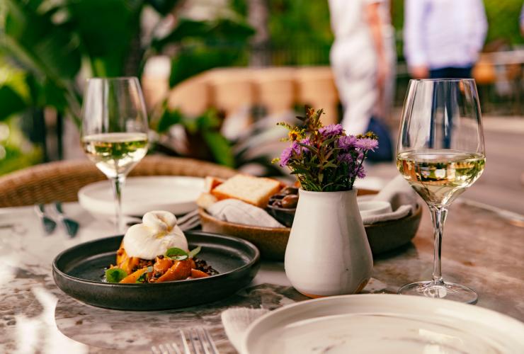 A plated dish and filled wine glasses on a table with a floral vase © Peats Bite