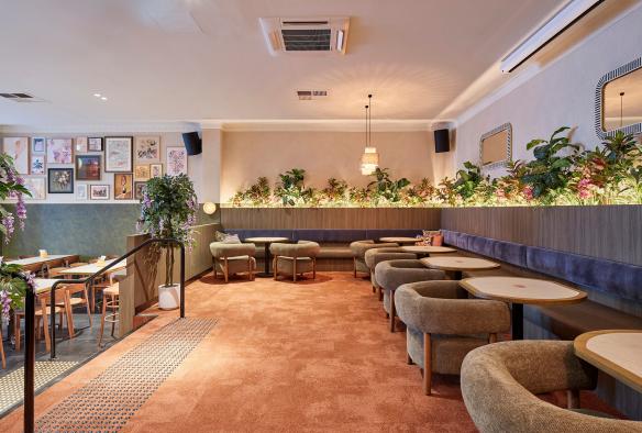 A view of Lil’s Hideout showing banquette seating, tables  and soft chairs on an upper level and tables and chairs below. © Shot by Thom