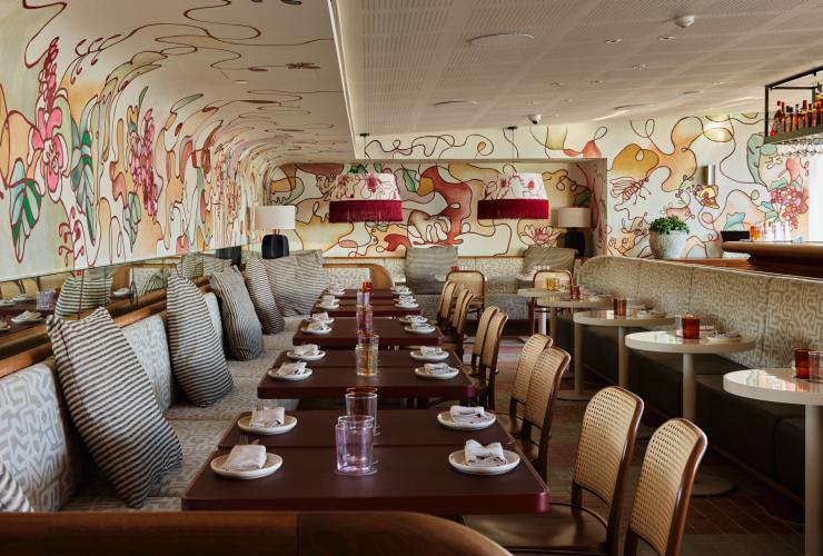 The eclectic, refined indoor space at Monica with banquette seating and a mural adorning the wall. © Steven Woodburn