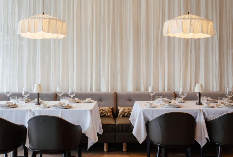 Banquette tables against a curtain with drop lamps above © Adam Gibson