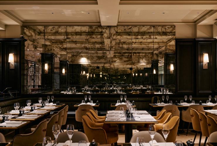 The exterior of Maison Bâtard showing a dark exterior on ground level and red brick exterior . Credit:  Alex Drewniak Mirror tiled walls reflect the dining tables and chairs in a black pillared restaurant © Pete Dillon