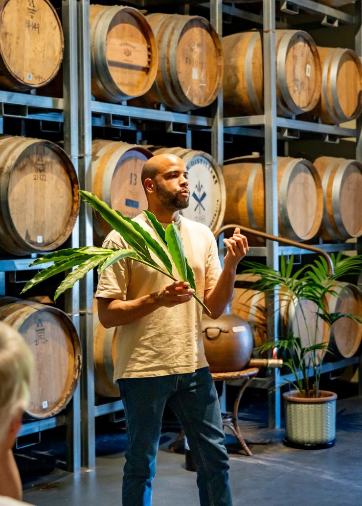 A Husk Distiller talks to guests in the distillery, standing in front of barrels. © Husk Farm Distillery