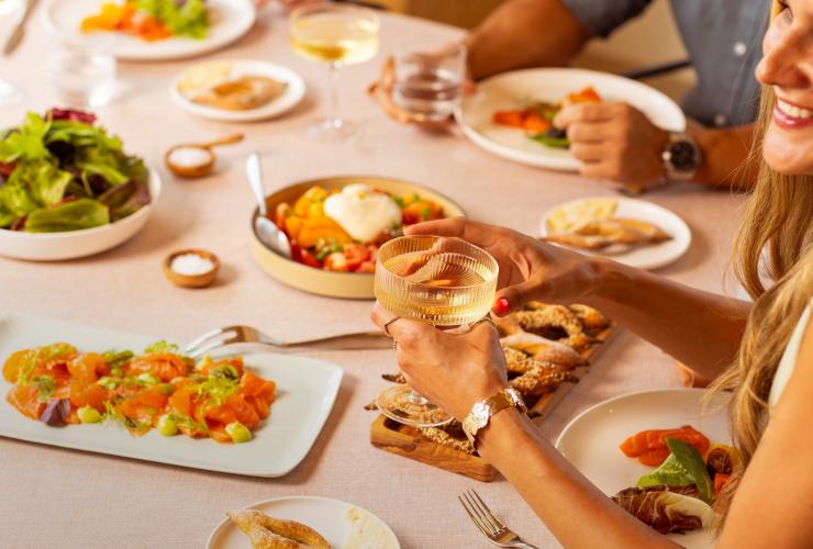 A table with platters of food and a woman with a glass in her hand. © Saltbox