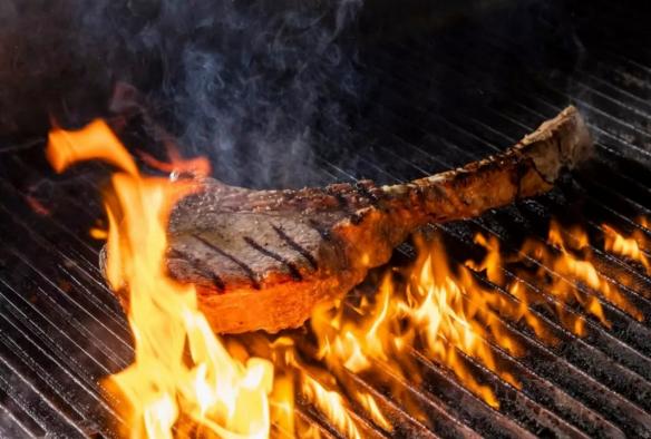 A tomahawk steak sizzles over a flaming grill © 7 Cutz  