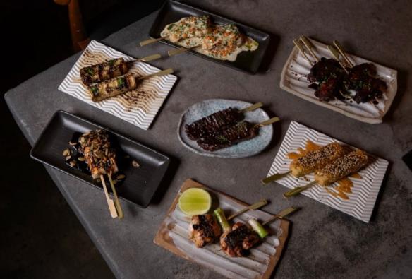 A table is set with a collection of fusion Japanese small plates including skewers and hand rolls © Shōtō