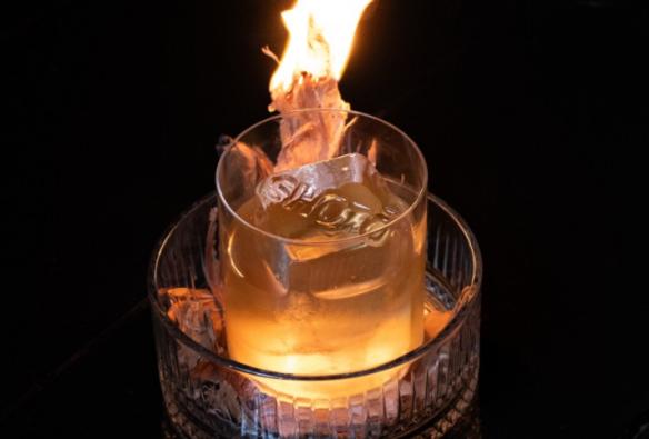 A cocktail is served in a bowl of coals, while a flame burns in the glass © Shōtō