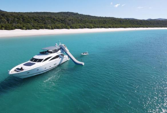 A luxury yacht is anchored near a white sandy beach, while people swim in the turquoise waters off the back of the boat © Sailing Whitsundays