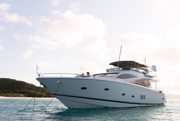 A shot taken from the water showing a luxury yacht anchored in a pretty bay, two people on deck enjoy the view of a setting sun © Sailing Whitsundays