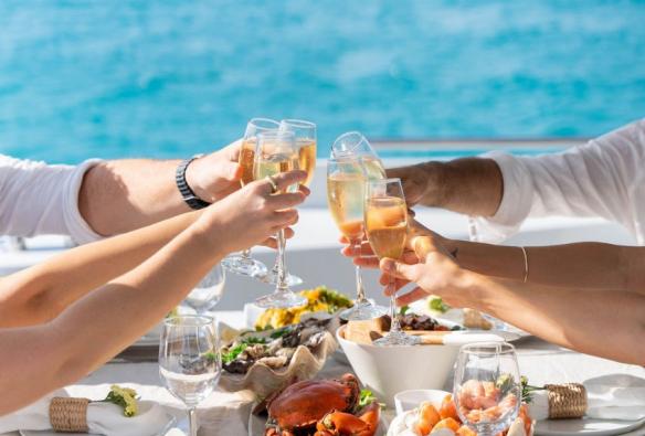 A close up of a table piled high with fresh seafood, while hands reach across to cheers glasses of sparkling wine © Sailing Whitsundays