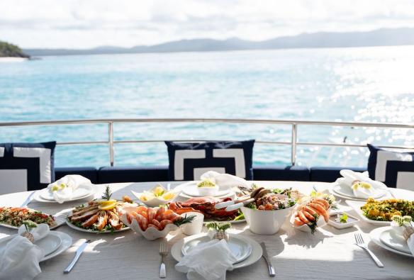 A table aboard a boat is set with mounds of fresh seafood and crisp white linens © Sailing Whitsundays